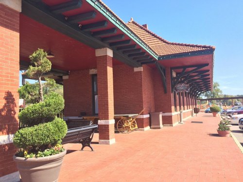 A brick building with a tiled roof, featuring planters and benches along a sunny walkway.