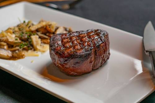 A perfectly grilled steak on a white plate, accompanied by sautéed mushrooms and herbs.
