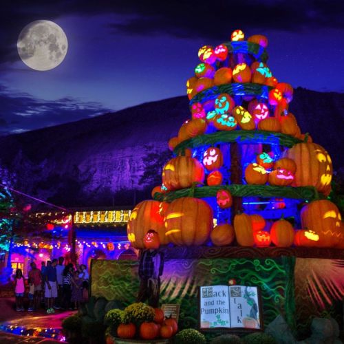 A vibrant display of illuminated pumpkins and decorations under a full moon, set against a mountain backdrop.
