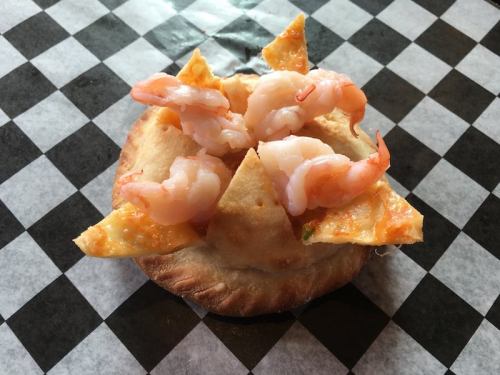 A small pastry topped with shrimp and tortilla chips, served on a black and white checkered paper.