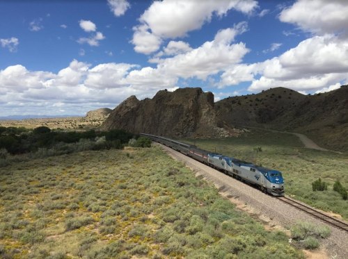 A train travels along a winding track through a rocky landscape under a cloudy sky.