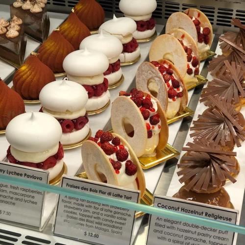 A display of elegant pastries, including pavlova, tart, and a hazelnut dessert, beautifully arranged in a showcase.