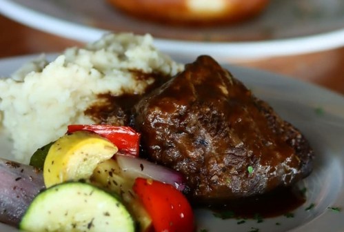 A plate featuring a piece of meat with gravy, mashed potatoes, and a colorful medley of grilled vegetables.