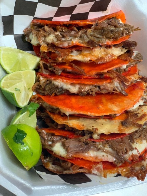 A stack of crispy tacos filled with meat and cheese, served with lime wedges on the side.