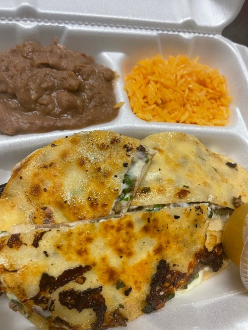 A takeout container with a quesadilla, refried beans, and orange rice, garnished with a lime wedge.