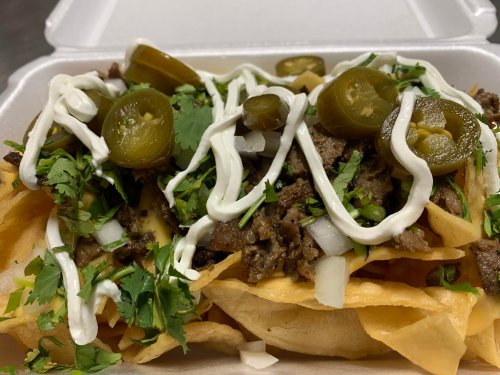 A close-up of nachos topped with seasoned beef, jalapeños, onions, cilantro, and drizzled with sour cream.