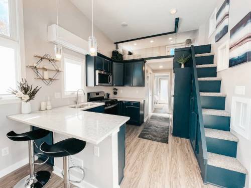 Modern kitchen with dark cabinets, a white countertop, and a staircase leading to an upper level. Bright and spacious design.