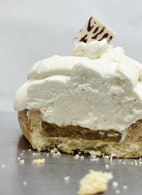 A close-up of a creamy dessert with whipped topping and a layer of filling, partially cut to reveal its interior.