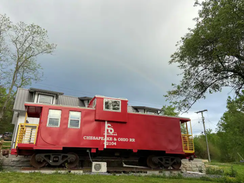 A red caboose from the Chesapeake & Ohio Railroad displayed next to a house under a cloudy sky.