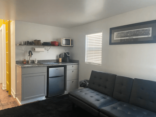 A modern kitchen area with a gray couch, countertop, microwave, and bright yellow wall in the background.