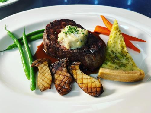 A plated meal featuring a grilled steak with herb butter, green beans, grilled potatoes, and a slice of savory pie.
