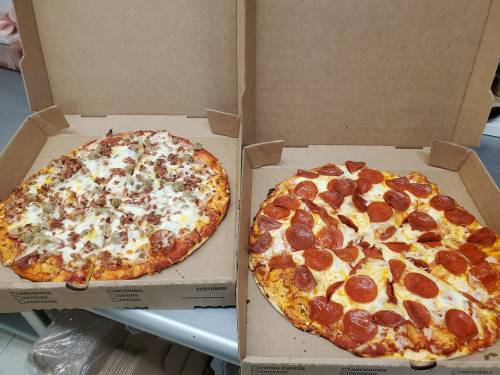 Two pizza boxes open, one with a meat pizza and the other with a pepperoni pizza, both freshly made.