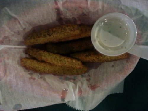 A basket of golden-brown fried zucchini sticks with a small cup of dipping sauce on the side.