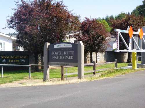 Sign for Powell Butte Nature Park, surrounded by trees and near a farm, with a road in the foreground.