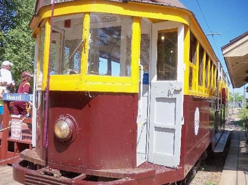 A vintage streetcar with a yellow and brown exterior, parked at a station under clear blue skies.