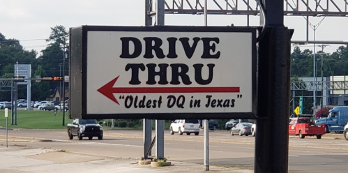 Sign for a drive-thru featuring "Oldest DQ in Texas" with an arrow pointing left.