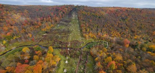Aerial view of a forested landscape with vibrant autumn colors and remnants of a rusted structure running through it.