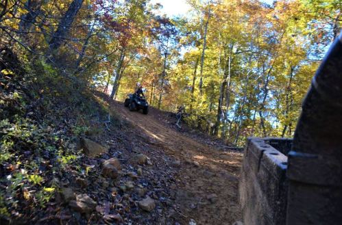 An ATV climbs a dirt trail surrounded by colorful autumn trees.