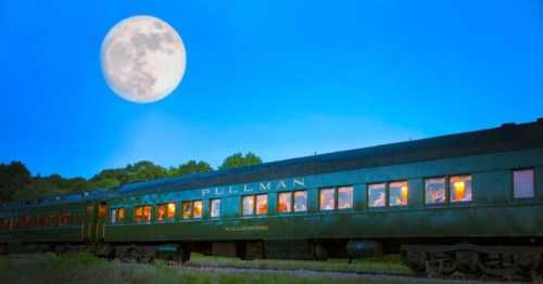 A vintage Pullman train under a bright full moon, with warm light glowing from its windows against a twilight sky.