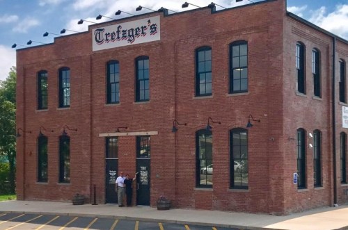 A brick building with large windows and a sign reading "Tretzer's," featuring two people standing at the entrance.