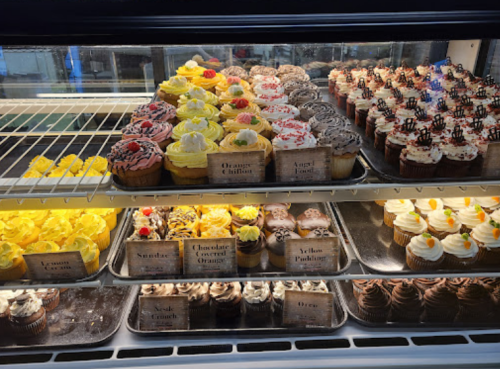 A display case filled with various colorful cupcakes, each labeled with different flavors.