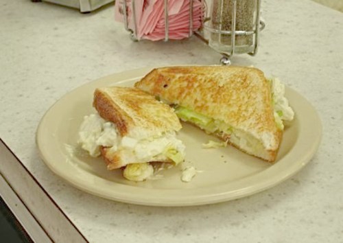 A toasted sandwich on a plate, partially eaten, with lettuce and a creamy filling.