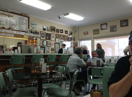A cozy diner interior with green chairs, a counter, and patrons enjoying their meals amidst vintage decor.