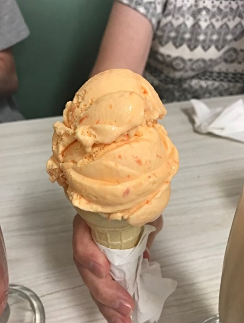 A hand holding a cone topped with two scoops of orange ice cream.