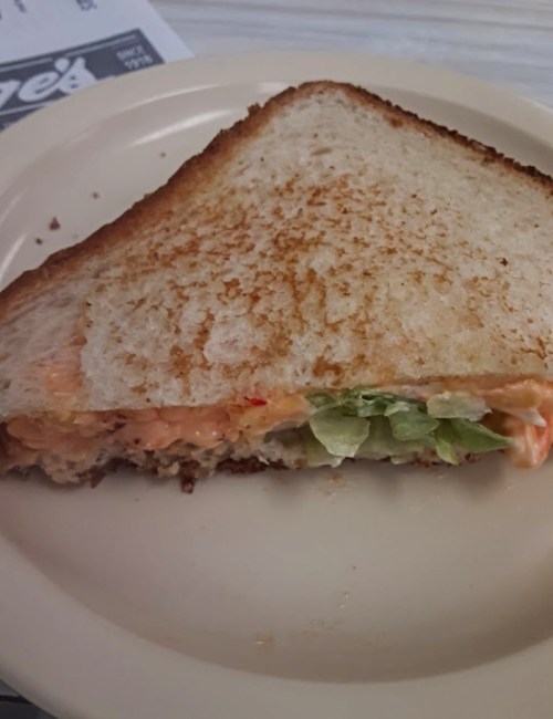 A toasted sandwich with a filling of shredded chicken and lettuce, served on a white plate.