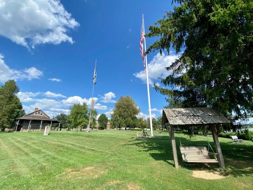 A grassy area with a swing, two flagpoles, and a building under a blue sky with scattered clouds.