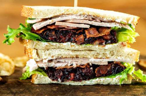 A stacked sandwich with turkey, bacon, lettuce, and cranberry spread, held together with a toothpick.