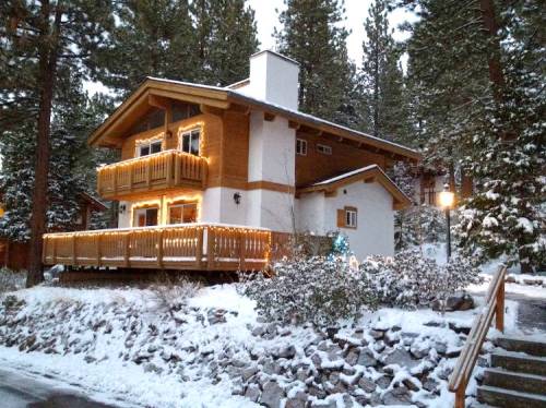 A cozy wooden house decorated with lights, surrounded by snow-covered trees and a snowy landscape.