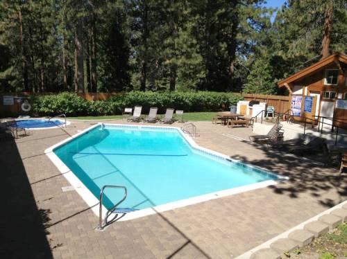 A clear swimming pool surrounded by lounge chairs and trees, with a wooden building in the background.