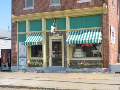 A brick storefront with green and white striped awnings, flowers, and a sign reading "OPEN" in the window.