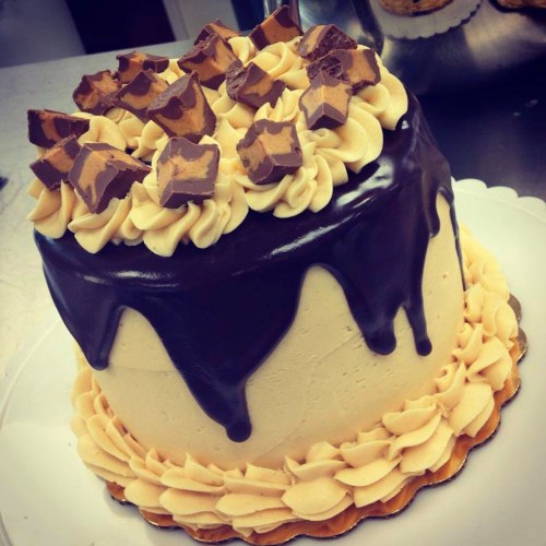 A layered cake topped with chocolate ganache, swirls of frosting, and chunks of chocolate candy.