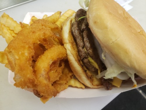 A close-up of a burger with two patties, cheese, lettuce, and onion rings, served with crinkle-cut fries.