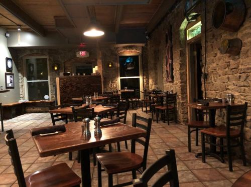 Cozy restaurant interior with stone walls, wooden tables, and chairs, softly lit for an inviting atmosphere.