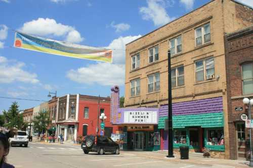 A vibrant street scene featuring colorful buildings, a banner overhead, and a marquee sign in a small town.