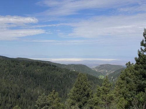 A panoramic view of green mountains under a blue sky, with a distant valley and hazy horizon in the background.