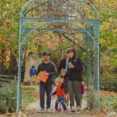 A family walks through a decorative archway surrounded by colorful autumn foliage.