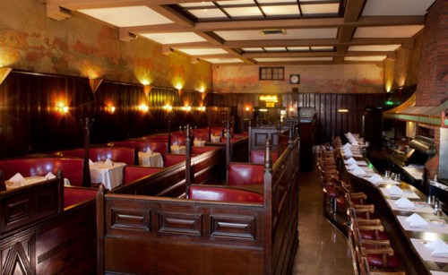 Interior of a vintage restaurant featuring wooden booths, elegant lighting, and a bar area.