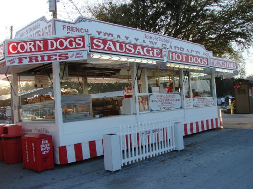 A food stand featuring signs for corn dogs, sausage, and French fries, with a red and white striped design.