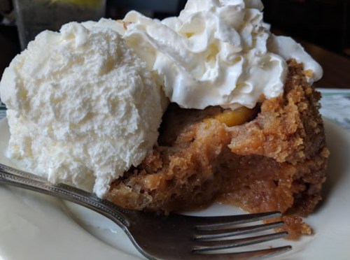 A slice of warm dessert topped with whipped cream, served with a scoop of vanilla ice cream on a white plate.
