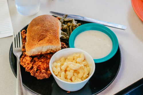 A plate with fried chicken, a roll, macaroni and cheese, green beans, and a bowl of gravy.