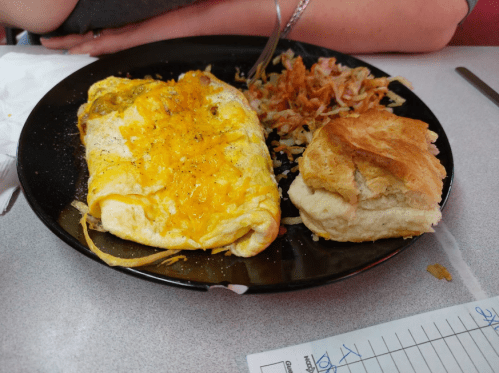 A plate with a cheesy omelet, hash browns, and a biscuit on a table.