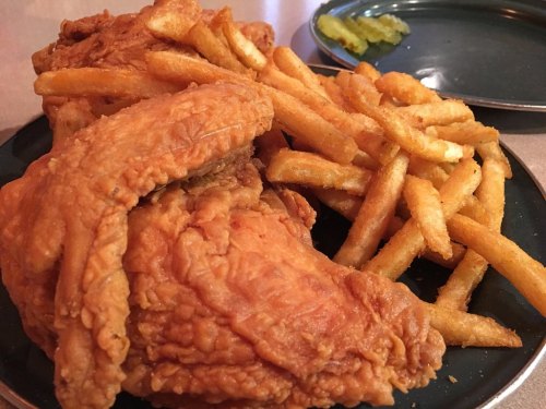 A plate of crispy fried chicken pieces served with golden French fries and a pickle on the side.