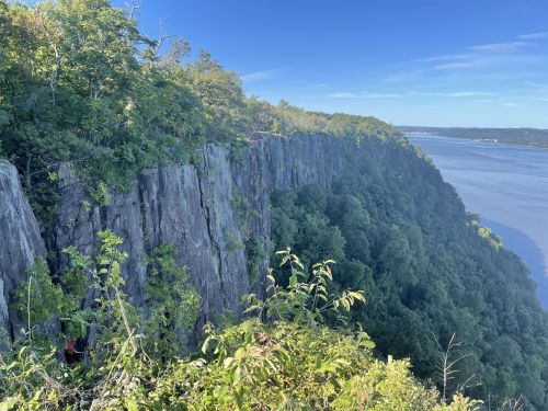 A scenic view of a rocky cliff covered in greenery, overlooking a river and blue sky.