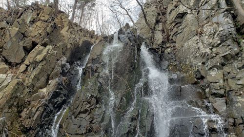A cascading waterfall flows down a rocky cliff surrounded by bare trees and rugged terrain.