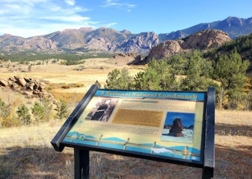 A sign about a national natural landmark in a scenic landscape with mountains and grassy fields in the background.