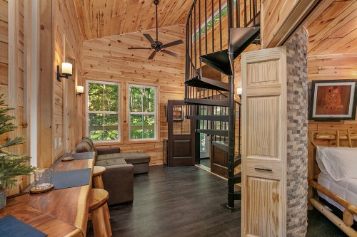 Cozy wooden interior of a cabin featuring a spiral staircase, seating area, and large windows with natural light.